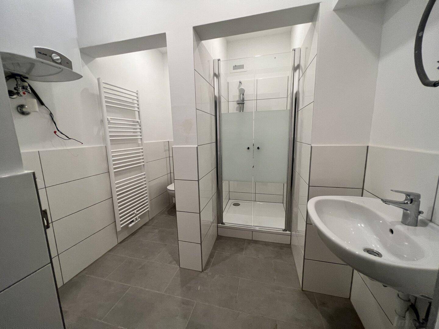 Modernes Badezimmer mit grauen Fliesen, Duschkabine, Waschbecken und beheiztem Handtuchhalter.