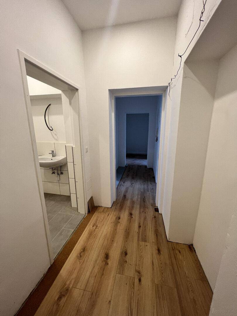 Heller Flur mit neu verlegtem Laminatboden, der zu verschiedenen Zimmern und dem Badezimmer führt.