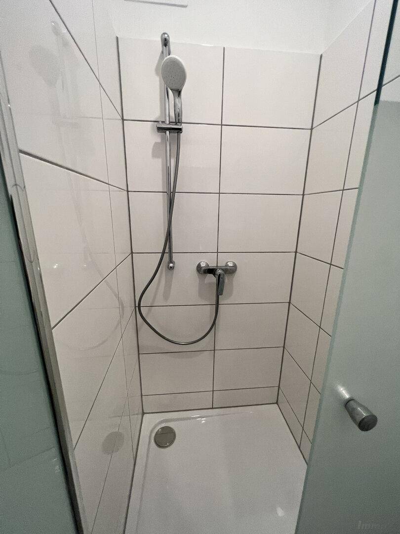 Moderne Duschkabine mit weißen Fliesen und einer einfachen Duscharmatur in einem hellen Badezimmer.