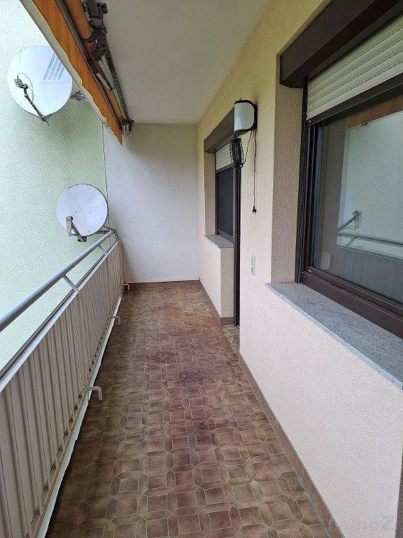 Langer Balkon mit Fliesenboden und Satellitenschüsseln an der Fassade.