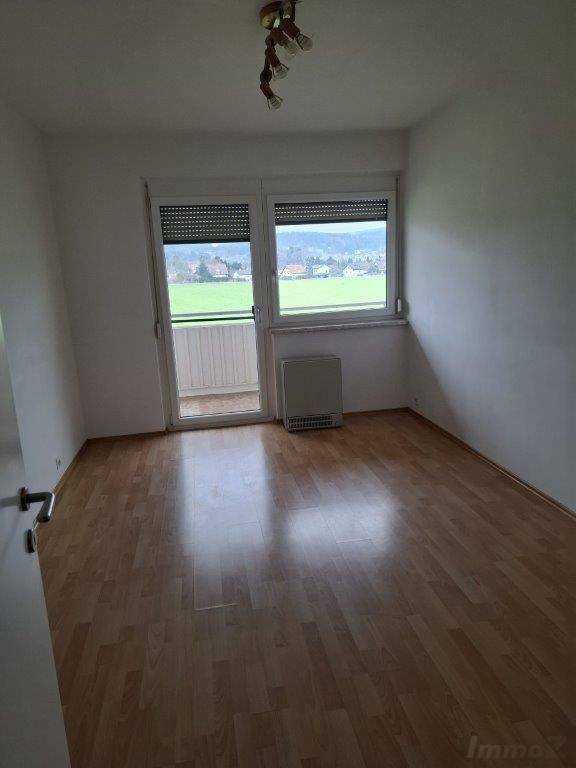 Helles Schlafzimmer mit Laminatboden und Zugang zu einem kleinen Balkon.