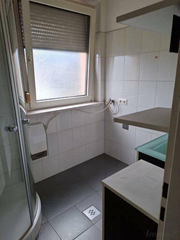 Badezimmer mit Duschkabine, Fenster und weißen Wandfliesen, funktional eingerichtet.