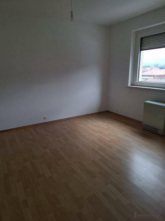 Leeres Wohnzimmer mit Laminatboden und Fenster mit Rollladen, bereit zur Einrichtung.