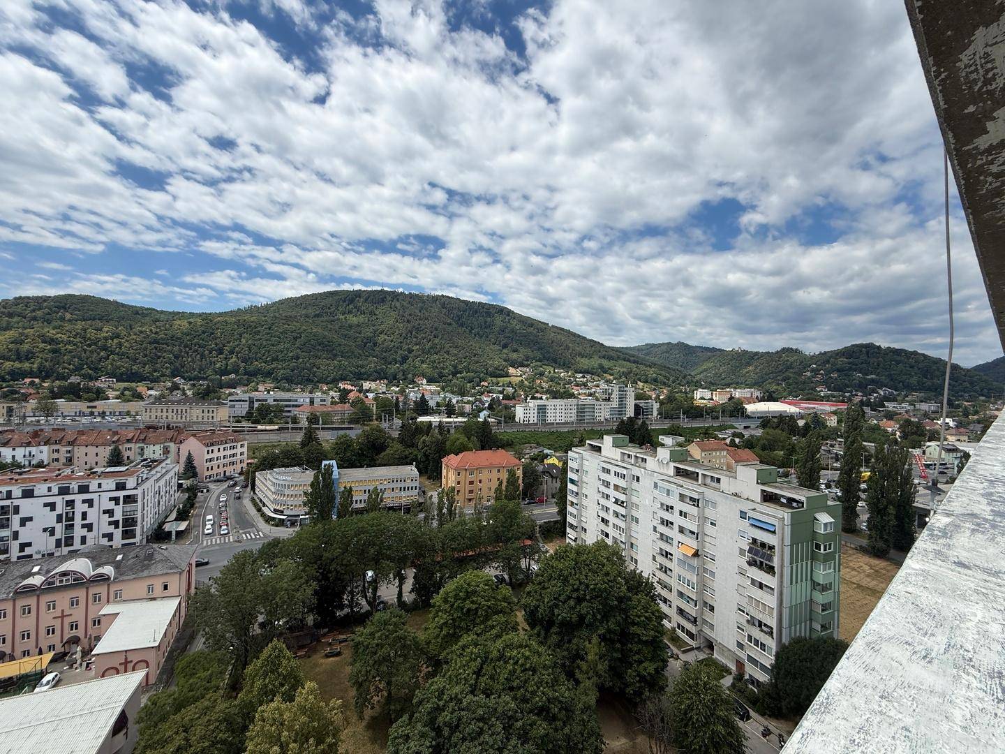 Aussicht über städtische Wohngebiete mit dichtem Baumbestand und bewaldeten Hügeln im Hintergrund.