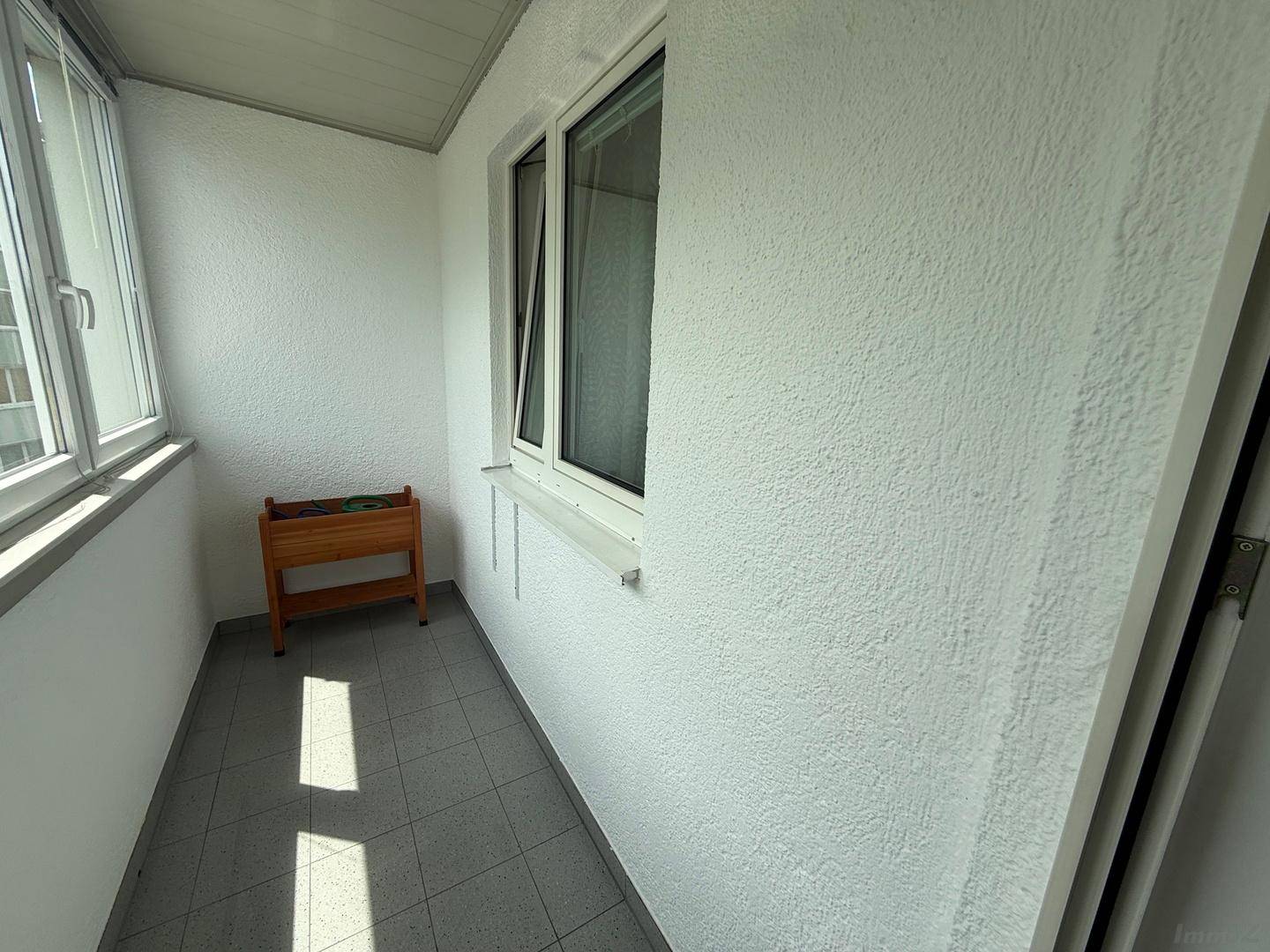 Verglaster Balkon mit hellen Fliesen und weiß gestrichenen Wänden, ideal für Pflanzen.