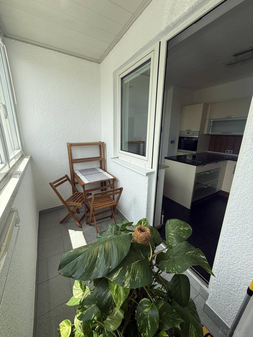Gemütlicher Balkon mit kleinem Holztisch, Stühlen und einer großen Pflanze, mit Zugang zur Küche.