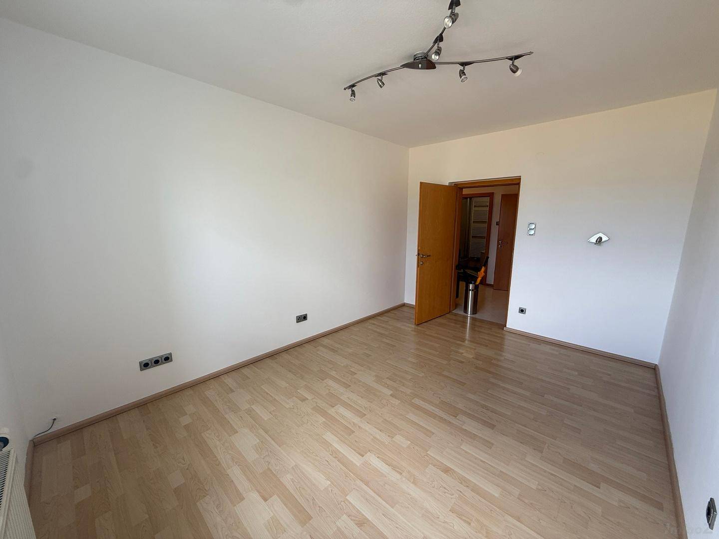 Leeres Zimmer mit hellem Laminatboden und weiß gestrichenen Wänden, bereit zur individuellen Gestaltung.