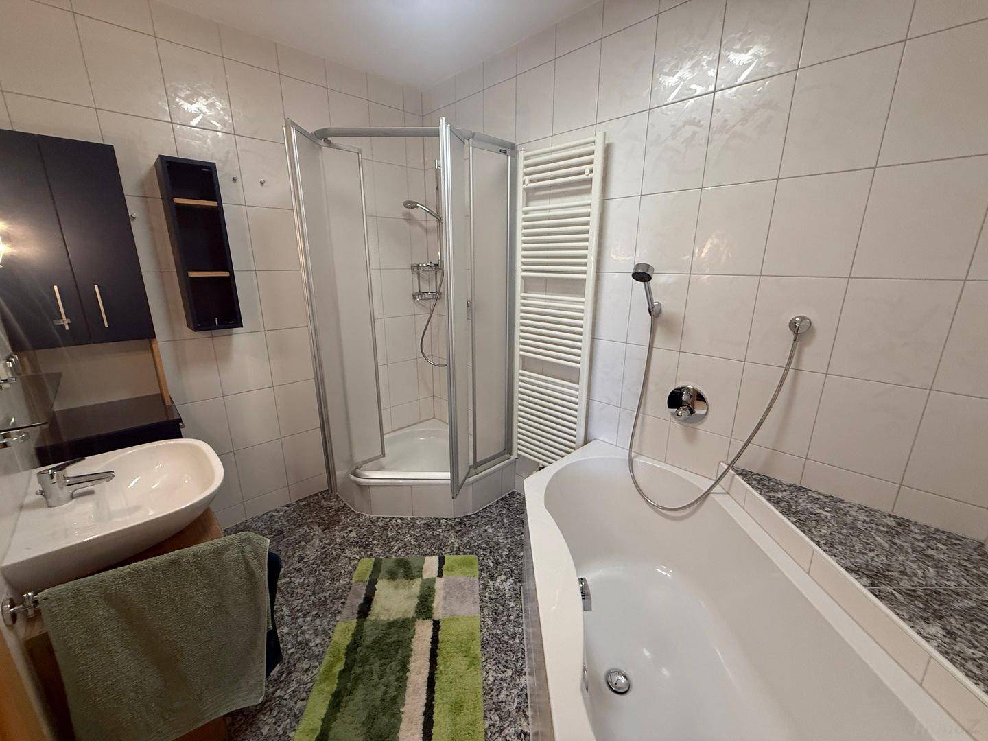 Badezimmer mit Duschkabine, Badewanne, Einzelwaschbecken und beheiztem Handtuchhalter.