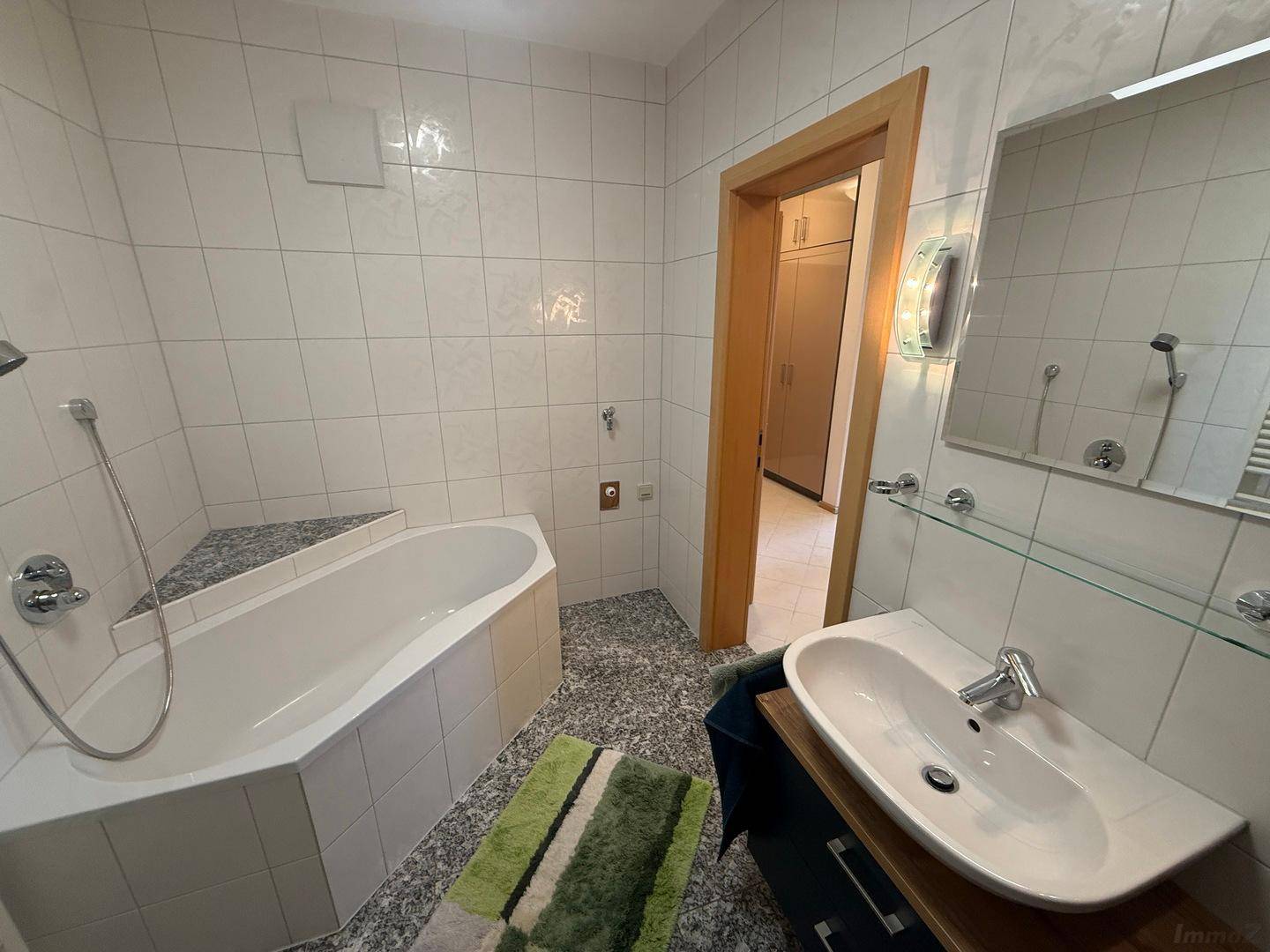 Modernes Badezimmer mit Badewanne, Waschtisch und Spiegel, alles in hellen Fliesen gehalten.