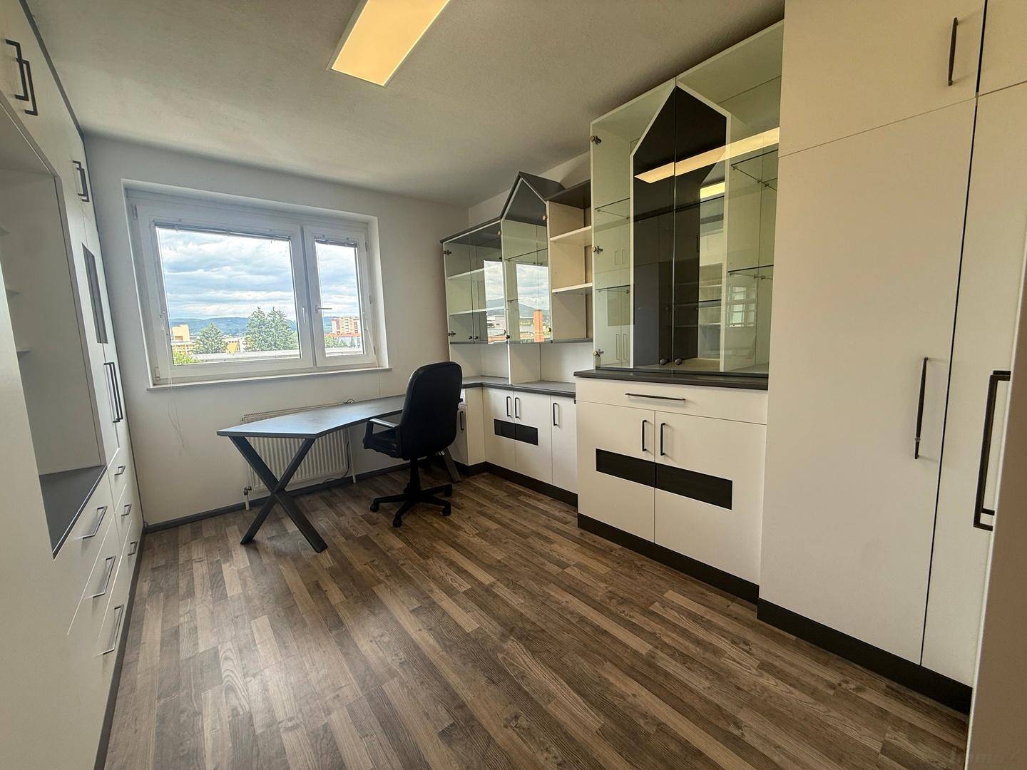 Helles Büro mit großem Schreibtisch, Bürostuhl und maßgefertigten Einbauschränken.