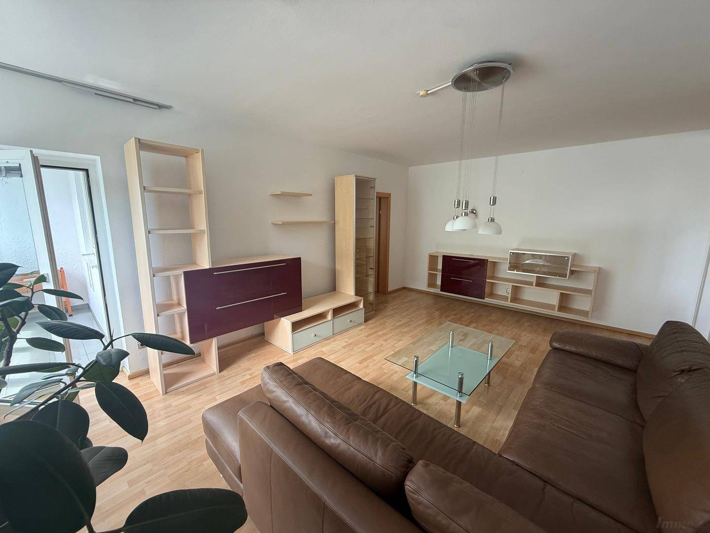Wohnzimmer mit Zugang zum verglasten Balkon, ausgestattet mit Sofa und Regalsystemen.