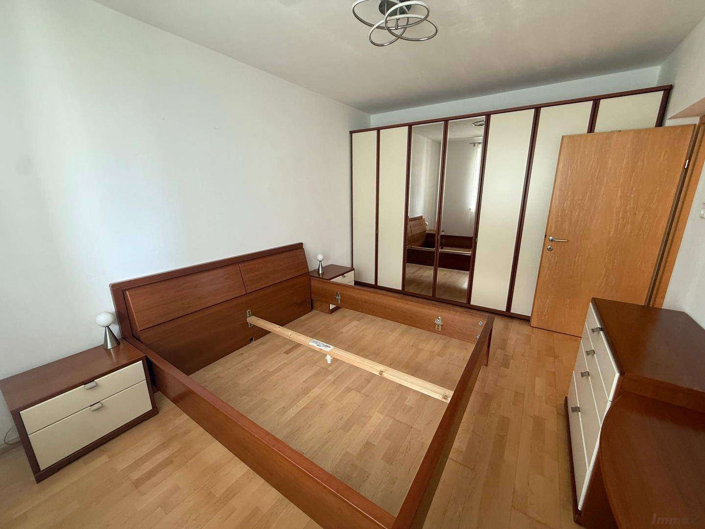 Schlafzimmer mit Holzbettrahmen, Nachttischen und einem großen Einbauschrank mit Spiegeltüren.