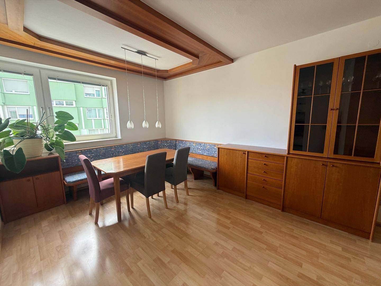 Heller Essbereich mit Holztisch, Eckbank, Holzschränken und dekorativen Deckenbalken.