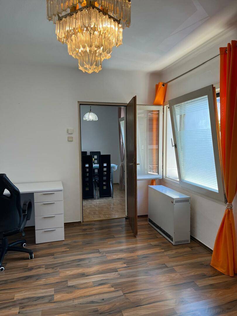 Helles Arbeitszimmer mit Schreibtisch, Fenster und Kronleuchter, Blick in den Essbereich.