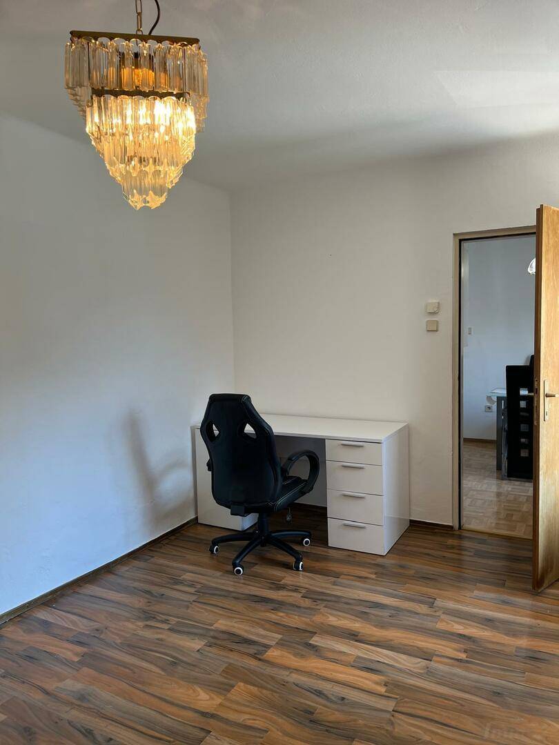 Arbeitszimmer mit Schreibtisch, Bürostuhl und einem eleganten Kronleuchter an der Decke.