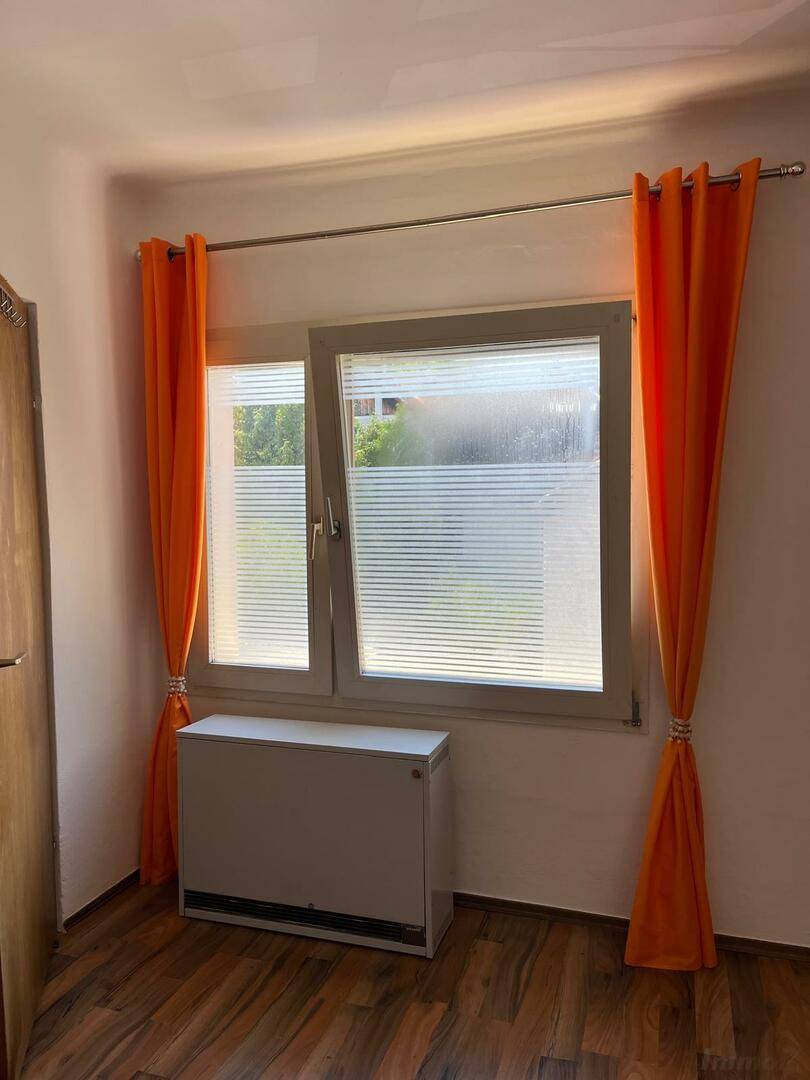 Heller Raum mit Fenster, orangefarbenen Vorhängen und Heizkörper.