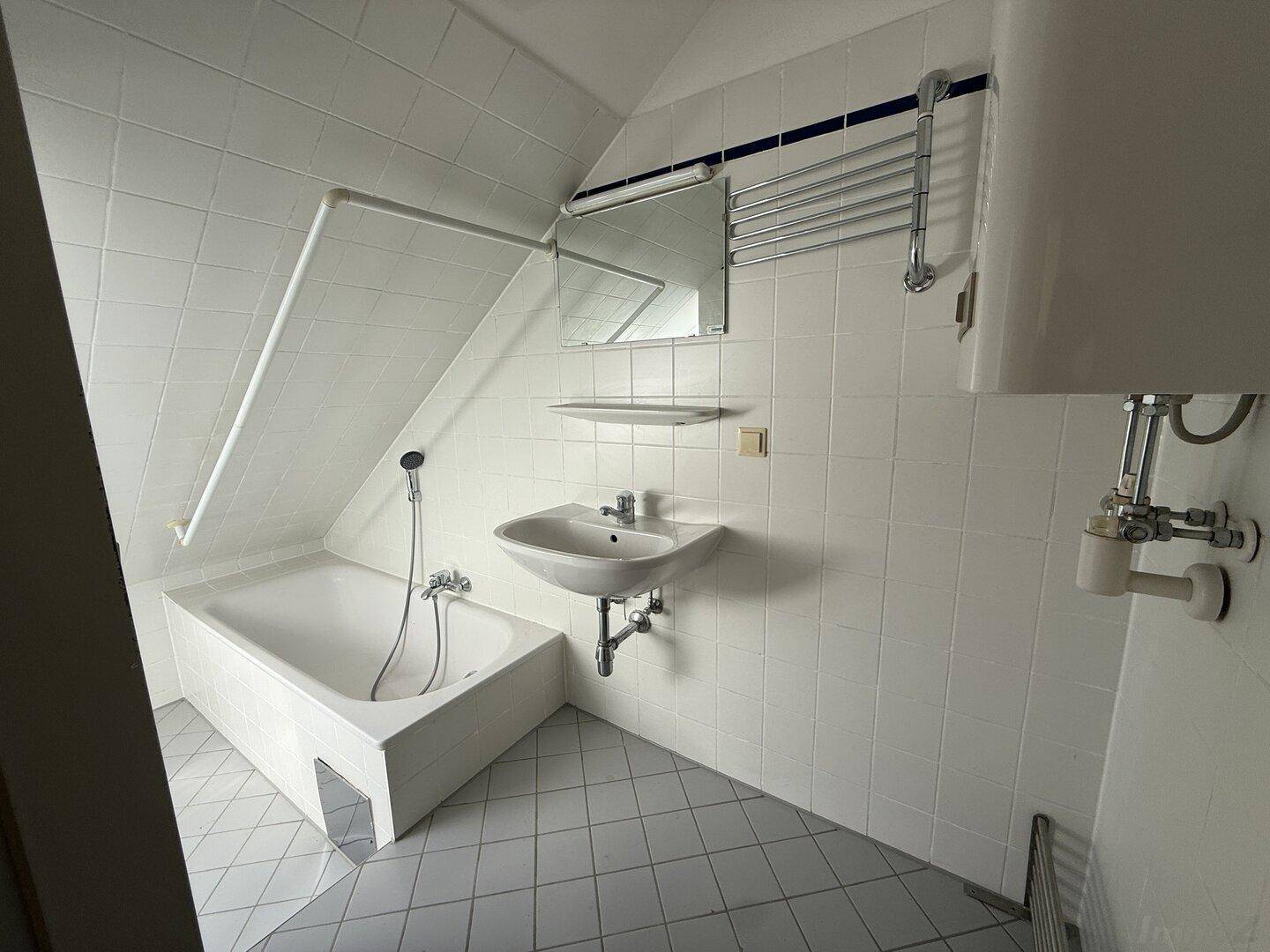 Badezimmer mit Badewanne, Waschbecken, weißen Fliesen und Dachschräge.