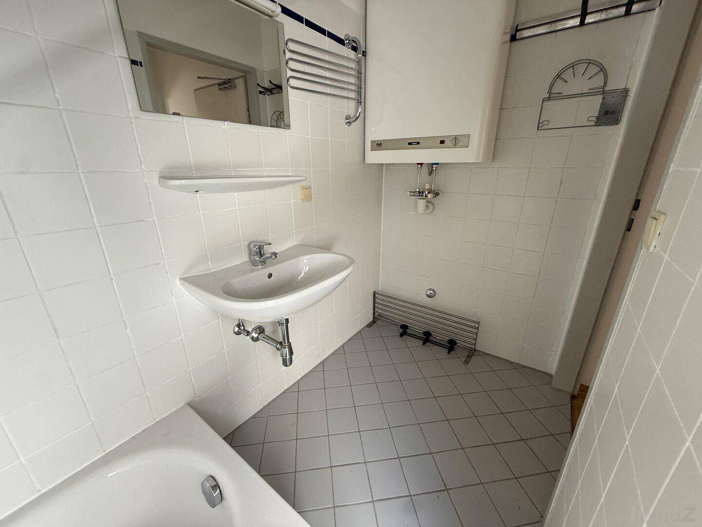 Detailansicht des Badezimmers mit Waschbecken, Spiegel und Handtuchheizkörper.