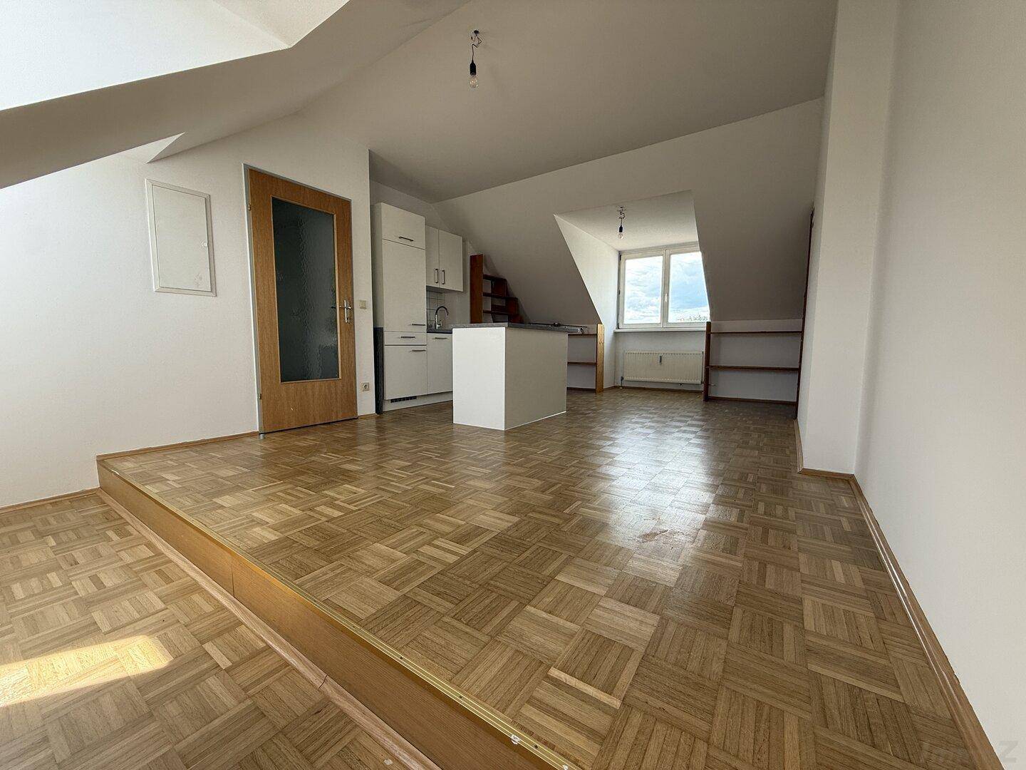 Offener Wohnbereich mit erhöhter Plattform, Parkettboden und integrierter Küchenzeile.