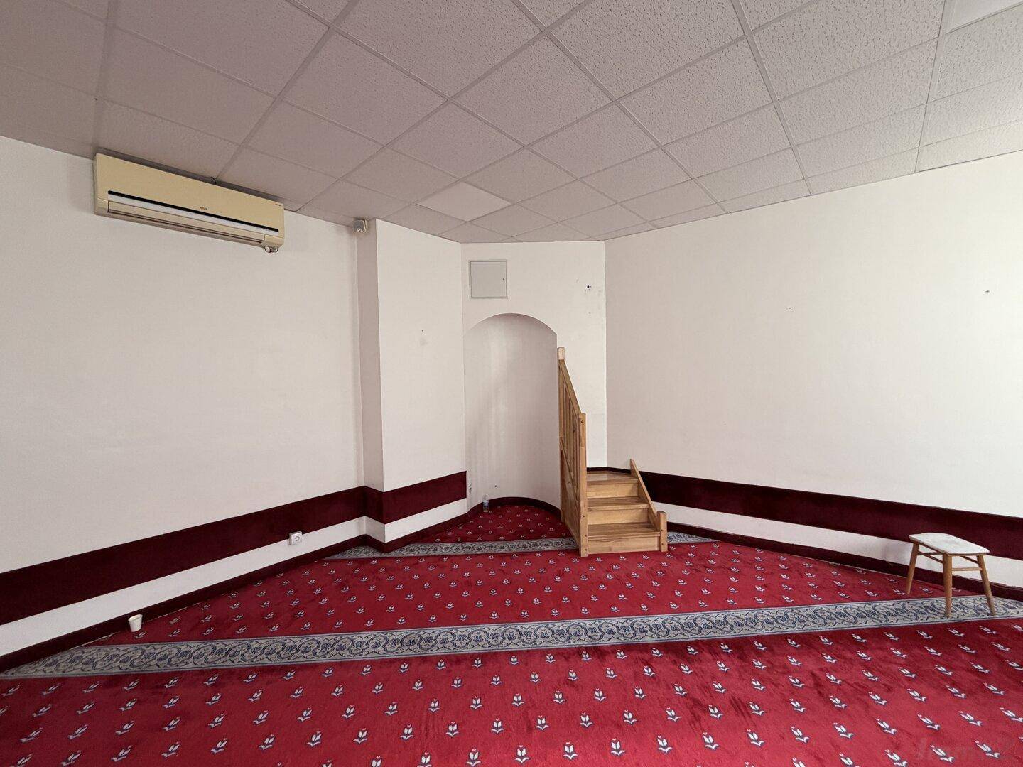 Innenraum mit rotem Teppichboden, weiß gestrichenen Wänden und einer kleinen Holztreppe zu einem erhöhten Bereich.