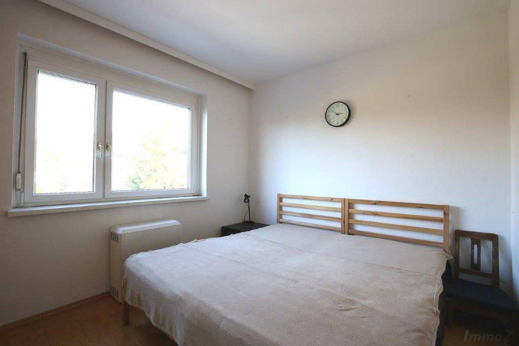 Schlichtes Schlafzimmer mit Doppelbett, Holzboden und großen Fenstern für viel Tageslicht.