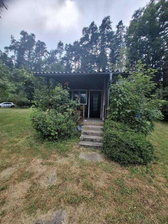 Rustikales Gartenhaus mit überdachter Veranda und Steinstufen, umgeben von dichtem Grün.