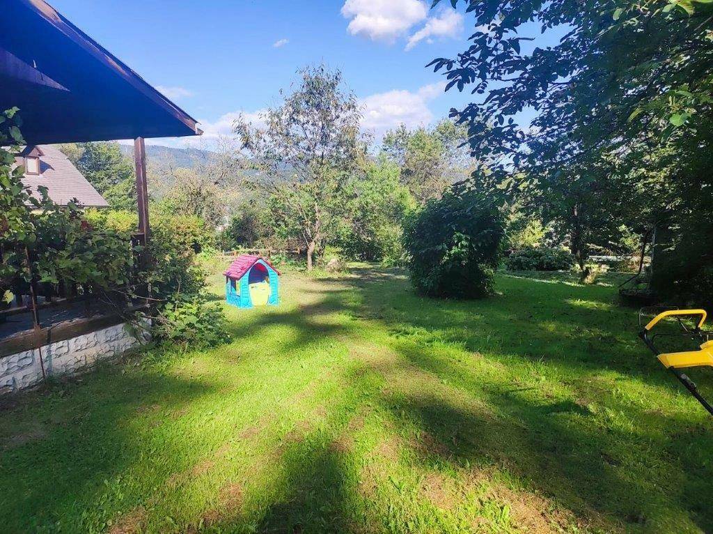 Sonniger Garten mit Rasenfläche, einem bunten Spielhaus und Blick auf die umliegenden Berge.