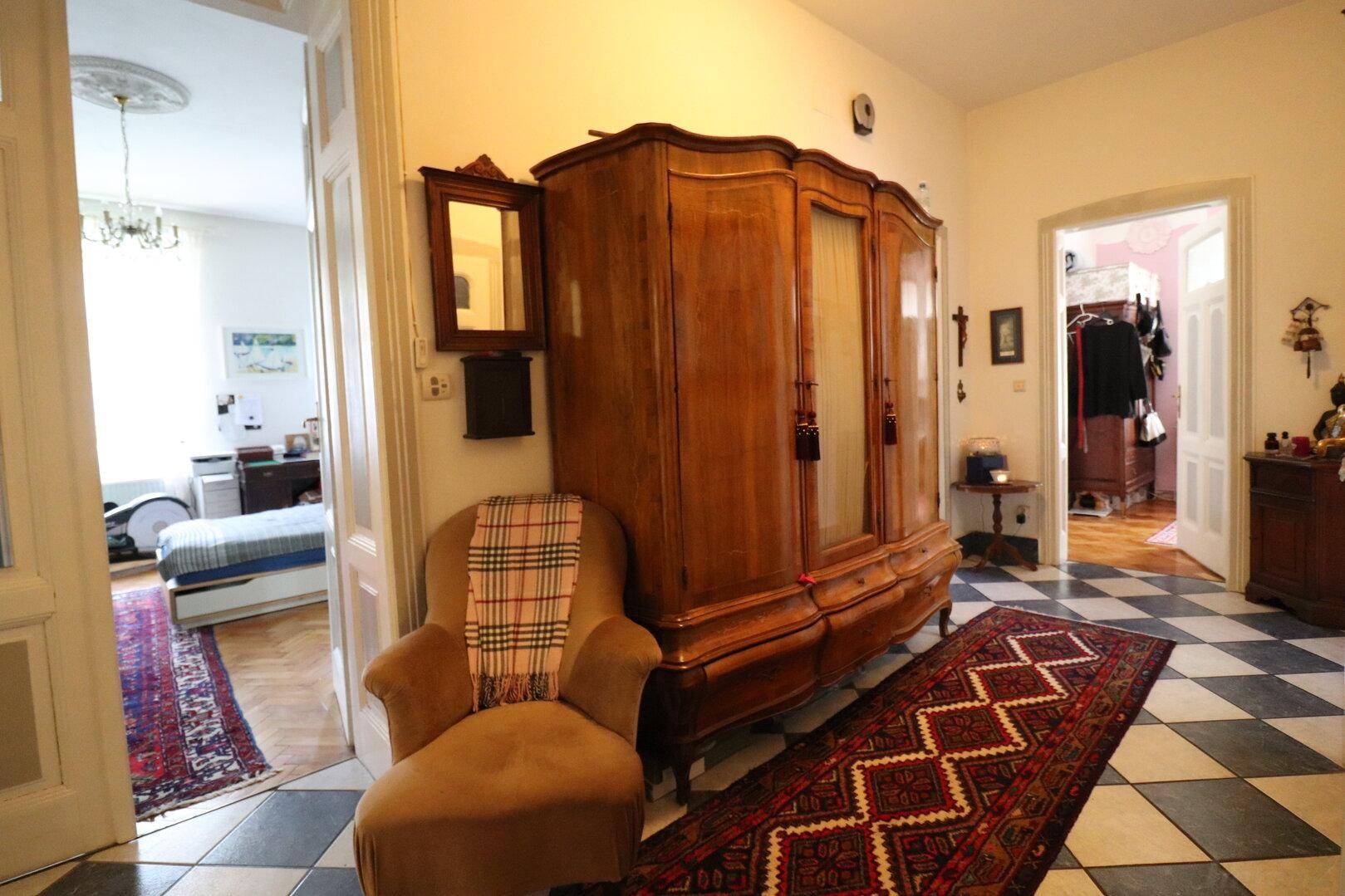 Geräumiger Flur mit Schachbrettmuster-Fliesenboden und antiker Holzgarderobe.