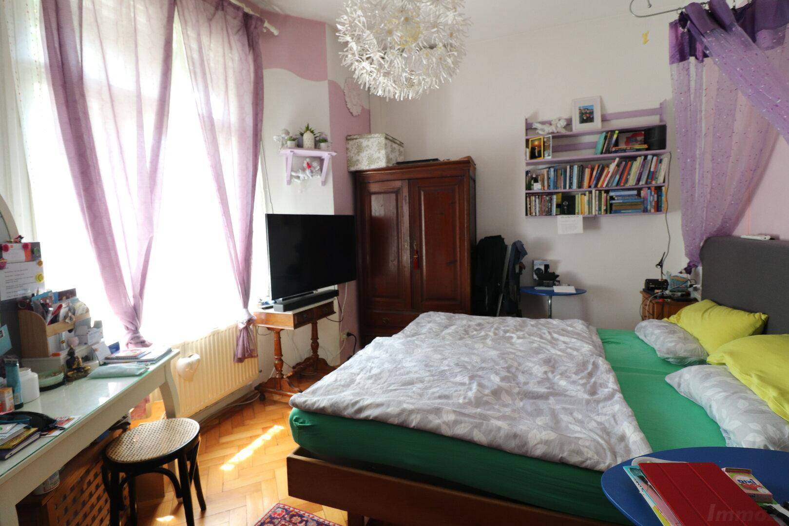 Schlafzimmer mit Parkettboden, lila Vorhängen und einem großen Bett.