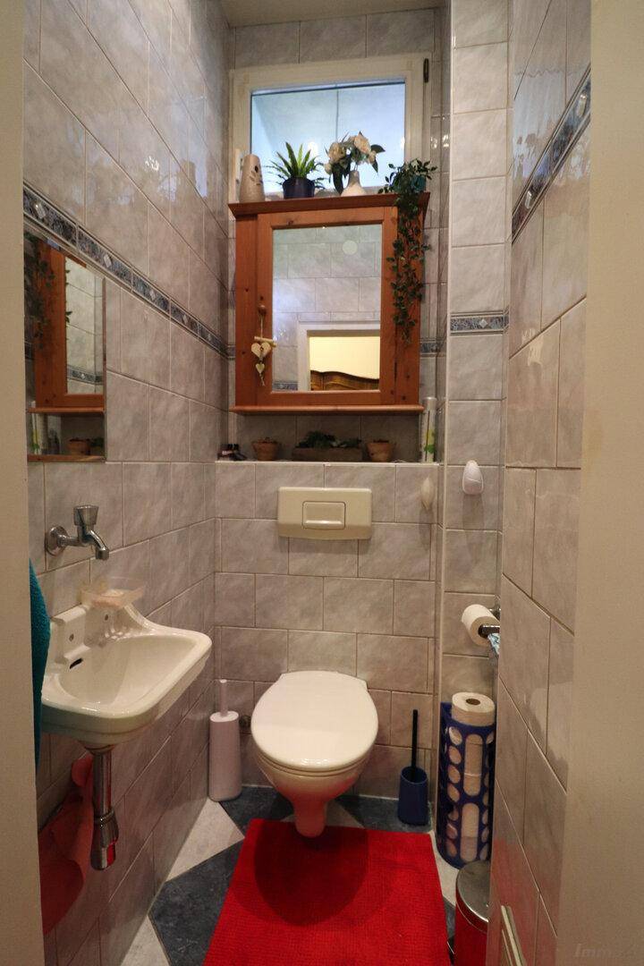 Kleines Gäste-WC mit hellen Fliesen, wandmontierter Toilette und Waschbecken.