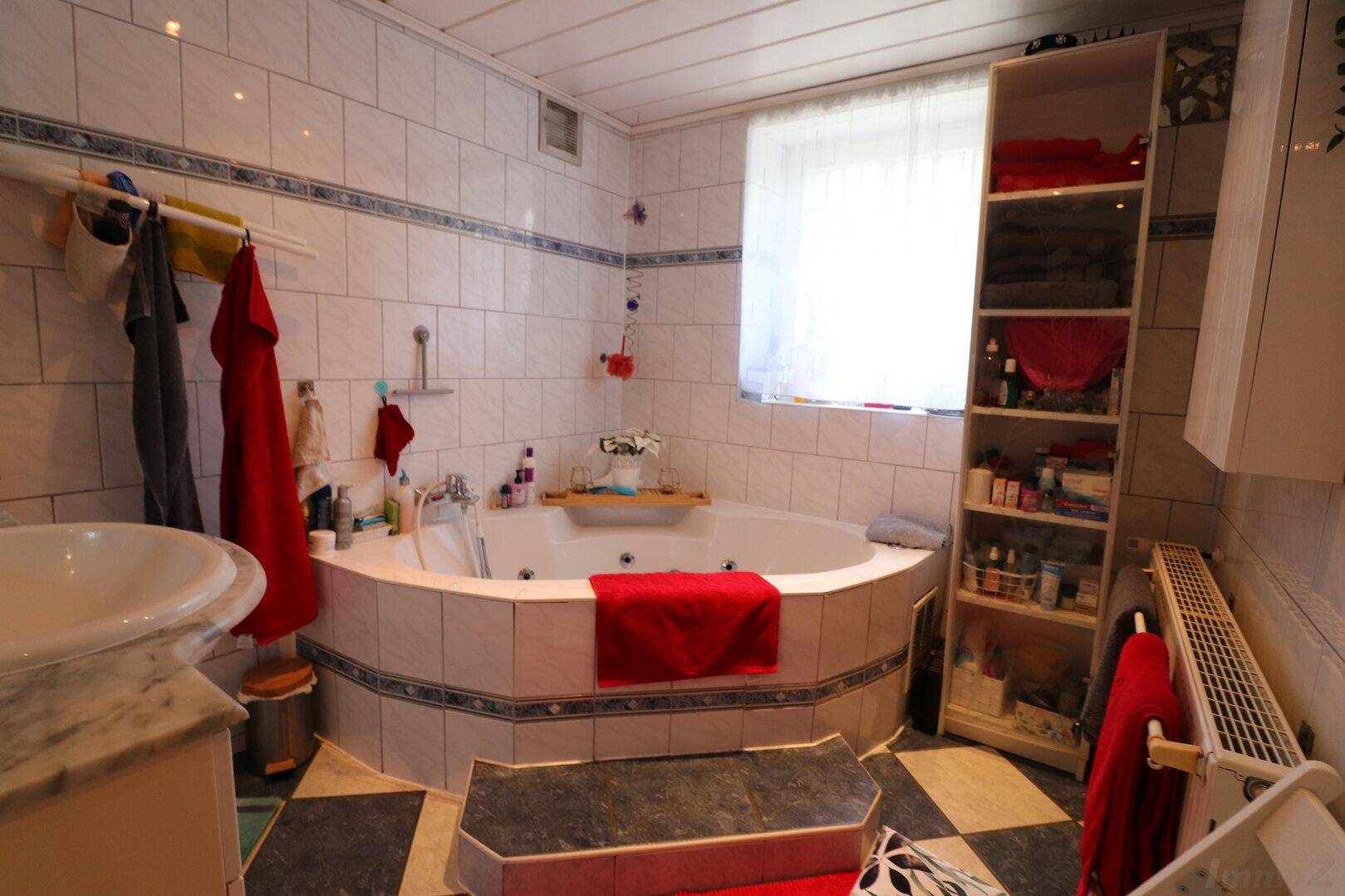 Geräumiges Badezimmer mit Eck-Whirlpool, hellen Fliesen und Fenster für Tageslicht.