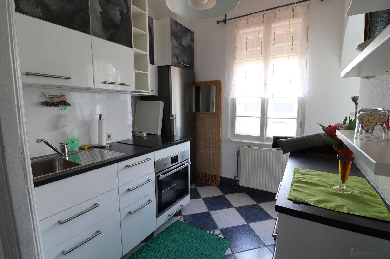 Kompakte moderne Küche mit weißen Hochglanzschränken, dunkler Arbeitsplatte und Fenster.