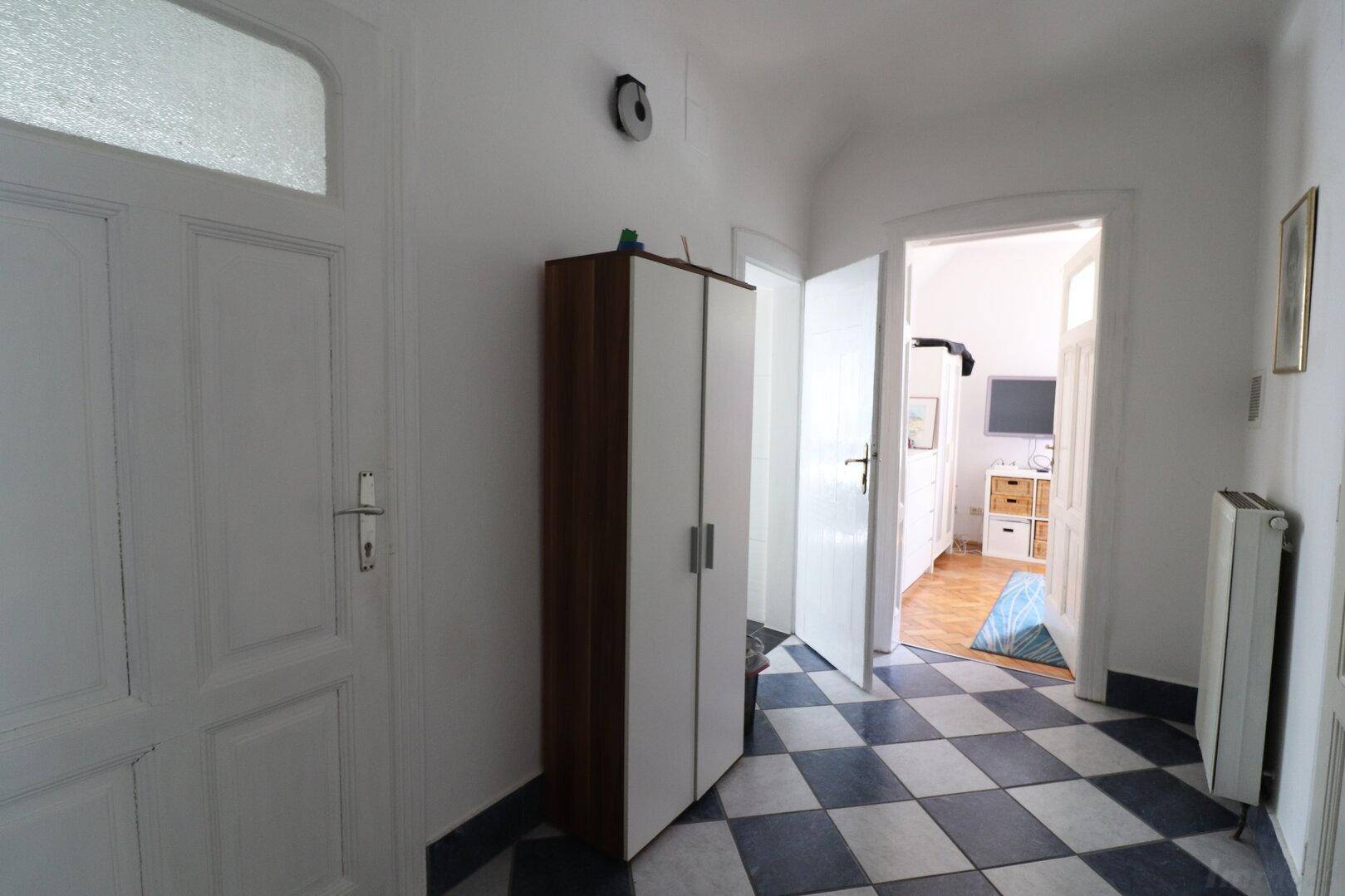 Flur mit Schachbrettmuster-Fliesenboden, Kleiderschrank und Zugang zu weiteren Räumen.