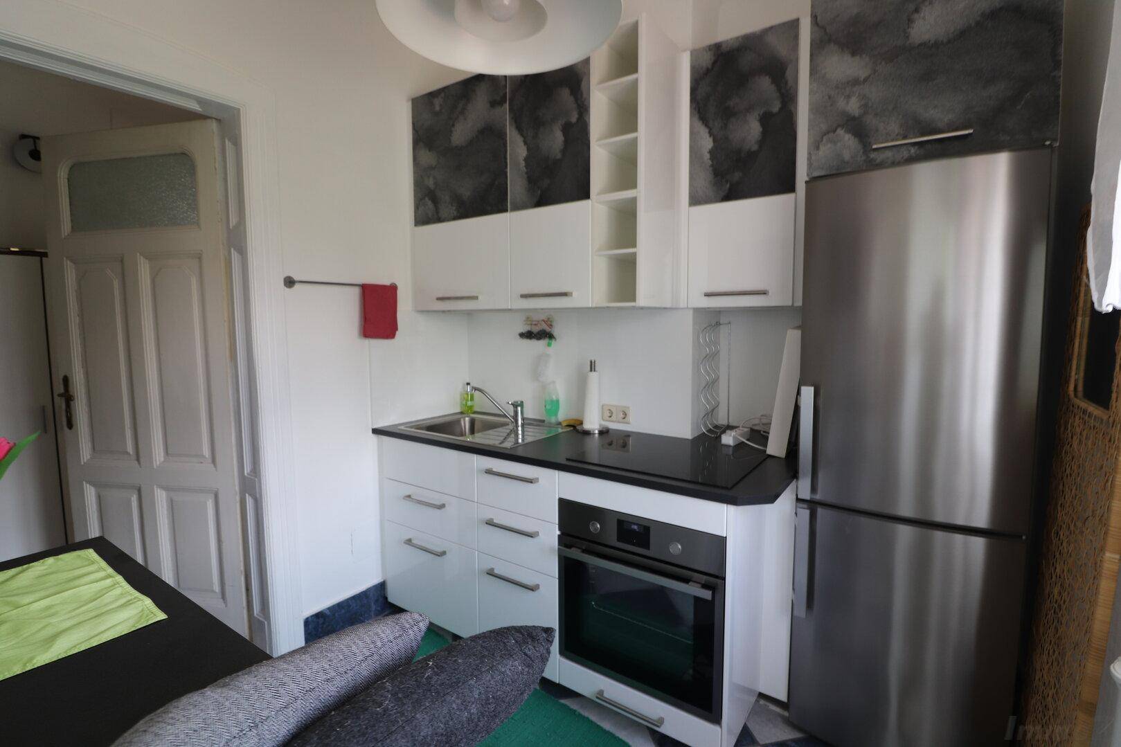 Kompakte Einbauküche mit weißen Schränken, integriertem Backofen und einem großen Kühlschrank.