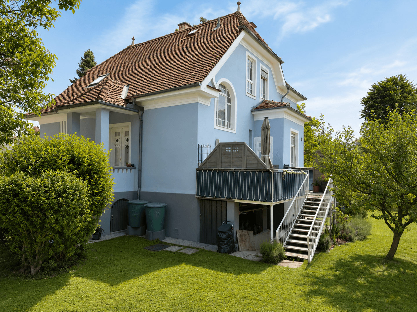 Rückansicht des Hauses mit großer Terrasse, Treppe zum Garten und viel Grün.