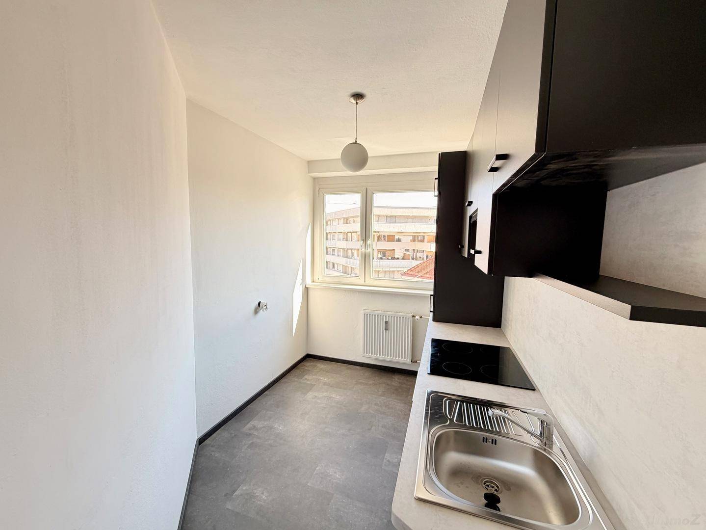 Moderne Küche mit dunklen Schränken, Spüle, Kochfeld und Blick aus dem Fenster.