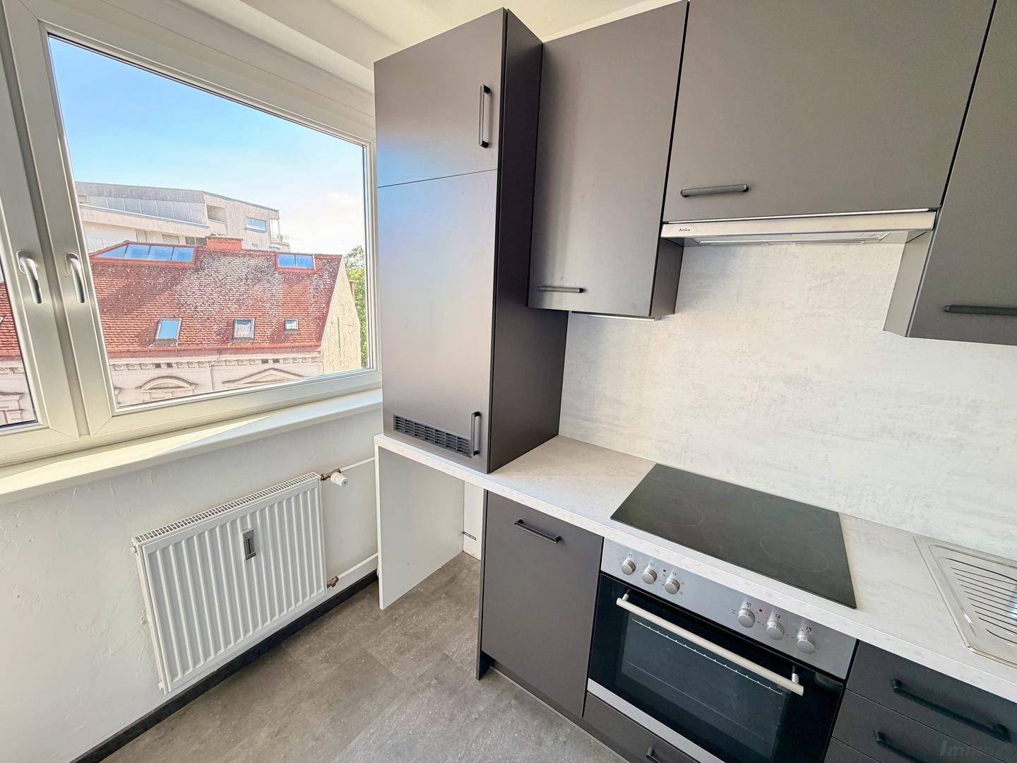 Neue Einbauküche mit grauen Schränken, integriertem Backofen und Kochfeld unter einem großen Fenster.