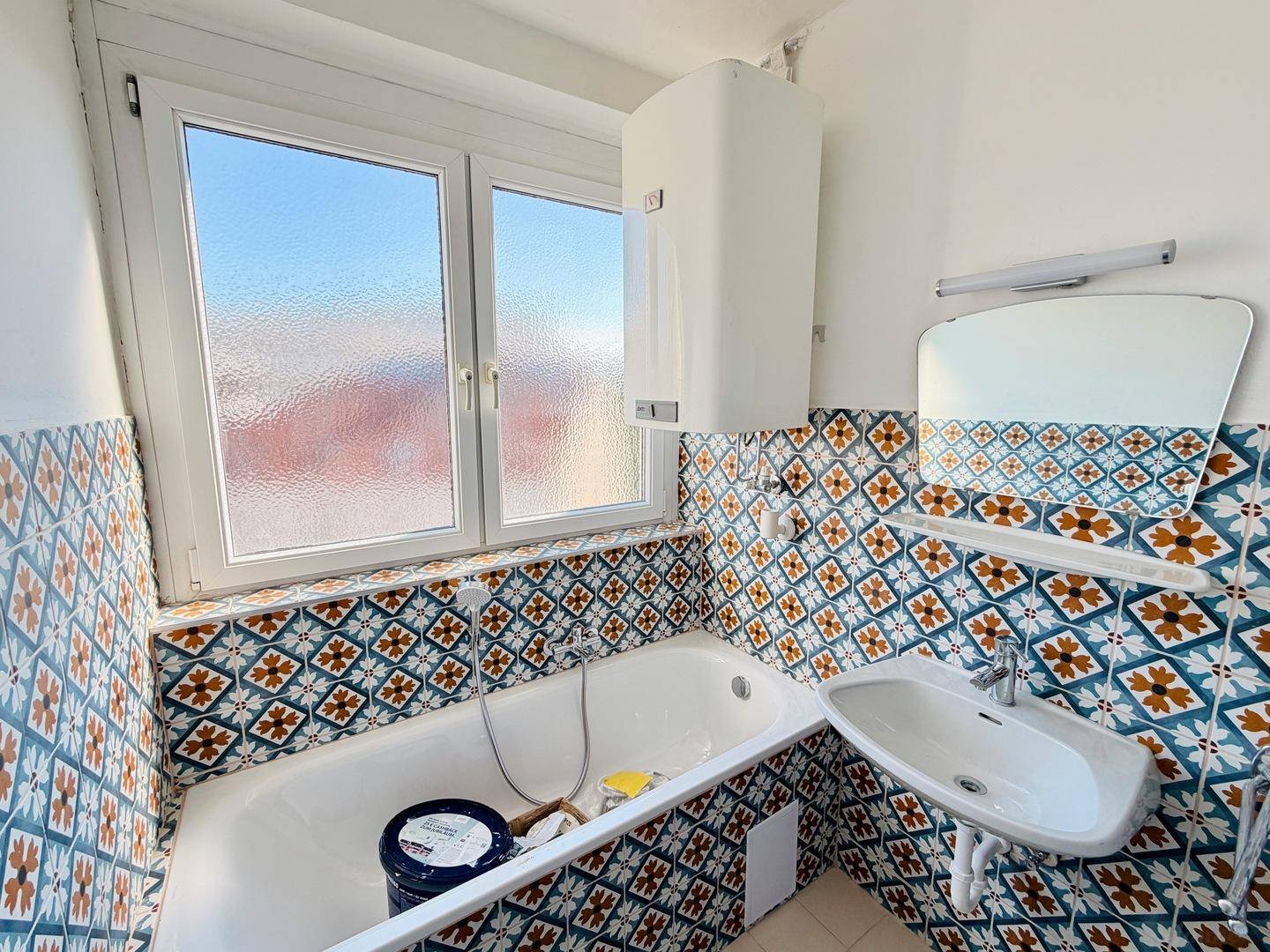 Badezimmer mit Badewanne, Waschbecken und auffälligen, gemusterten Fliesen sowie einem Fenster.