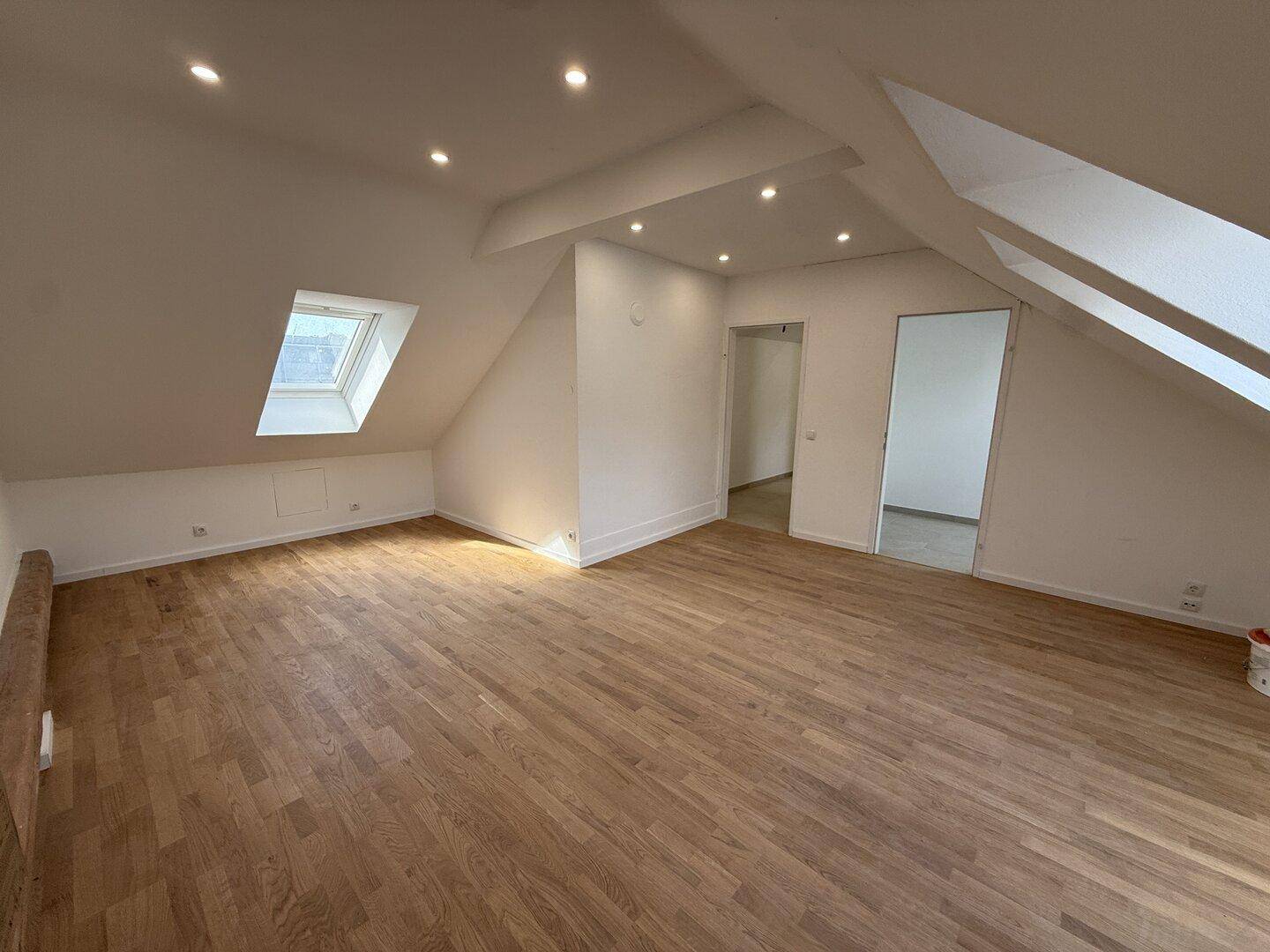 Heller Dachgeschossraum mit Holzboden, Dachfenstern und Zugang zu angrenzenden Zimmern.