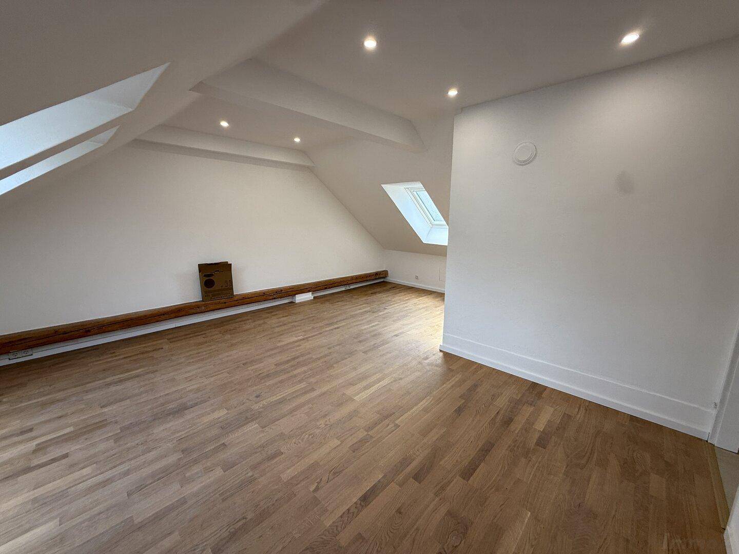 Weitläufiger Dachgeschossraum mit Holzboden, Dachfenstern und weiß gestrichenen Wänden.