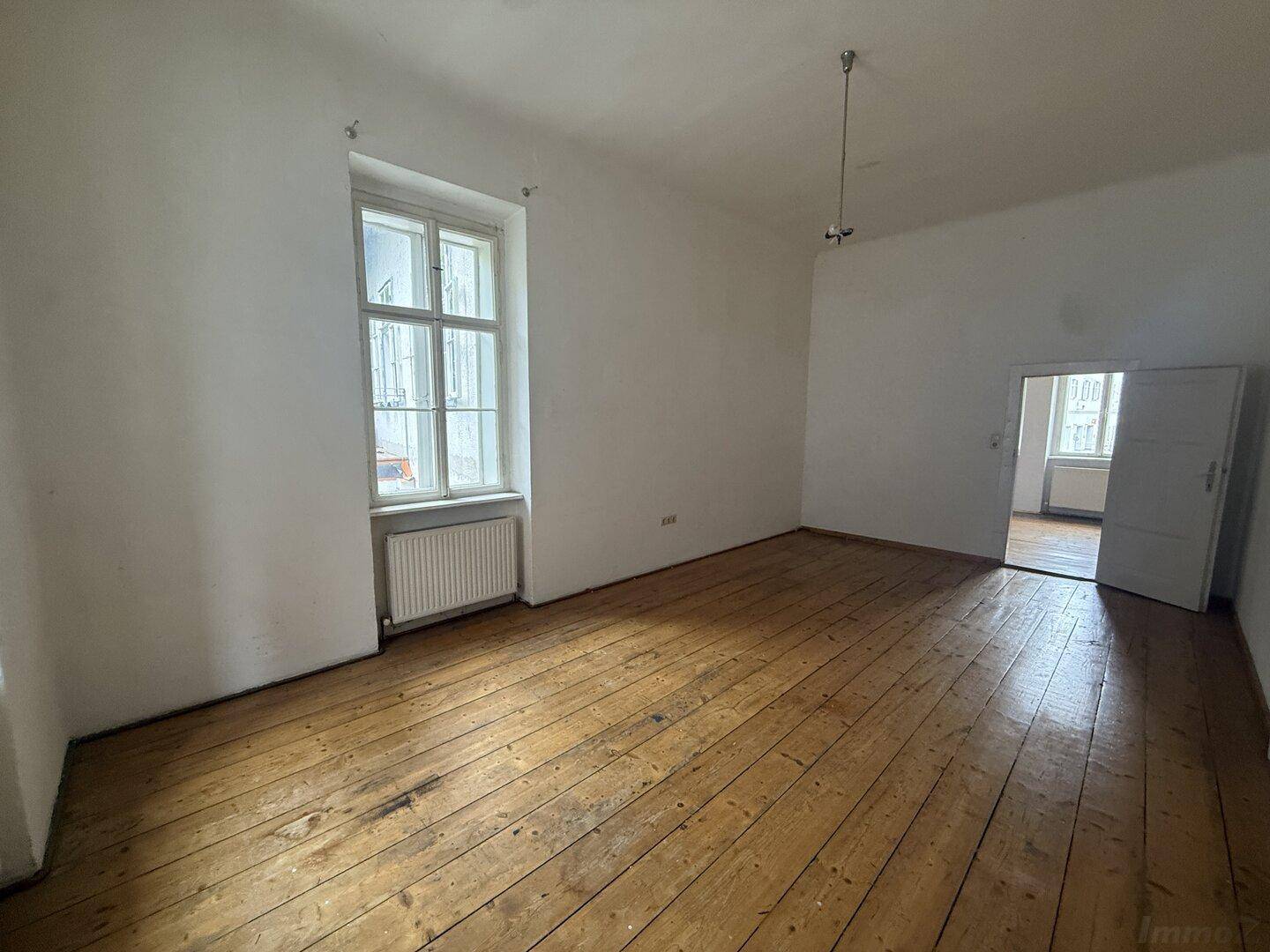 Helles Zimmer mit Holzdielenboden und Zugang zu einem weiteren Raum, bietet vielseitige Nutzungsmöglichkeiten.