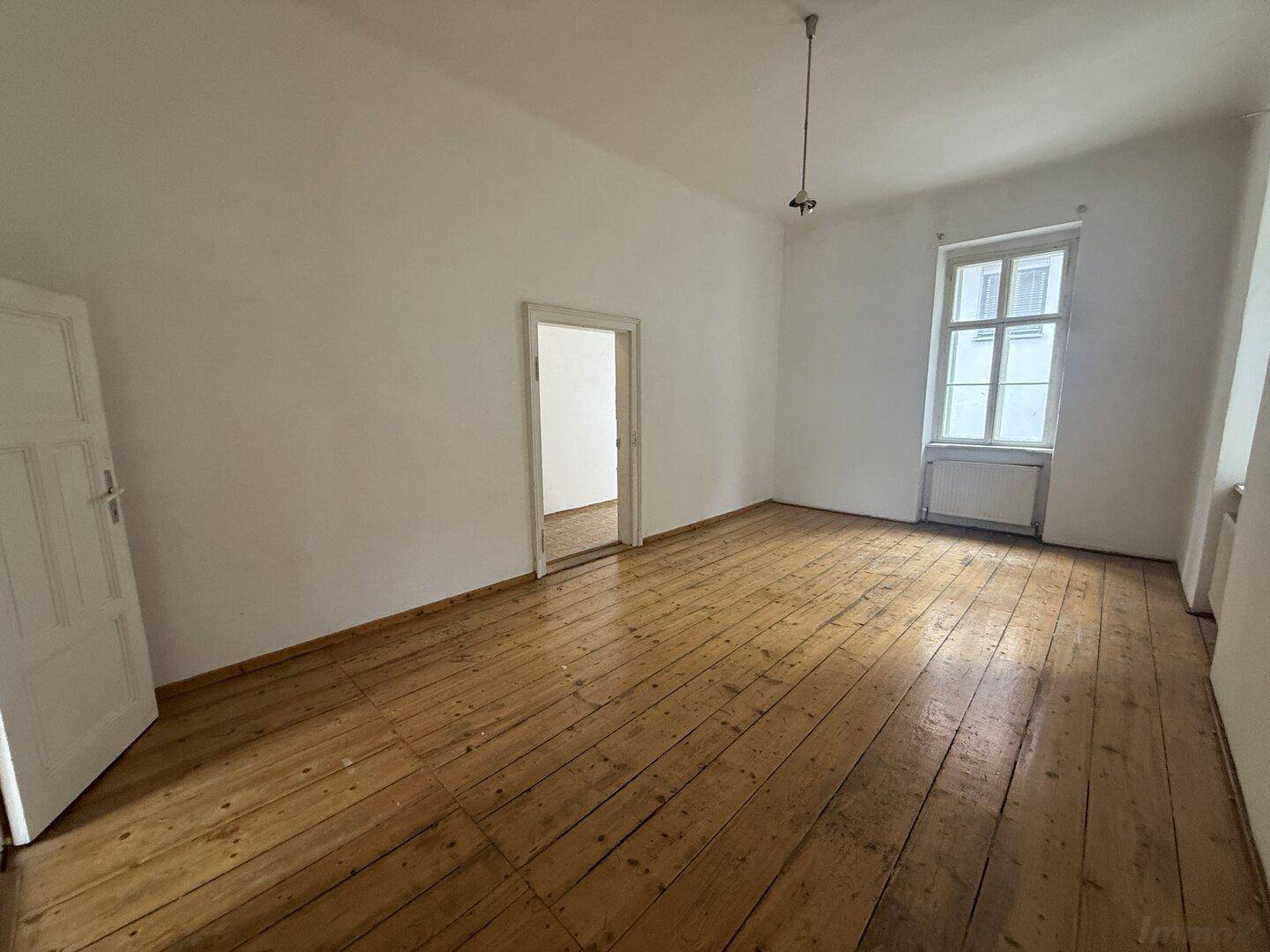 Geräumiges Zimmer mit Holzdielenboden und einem Fenster, das viel Tageslicht hereinlässt.