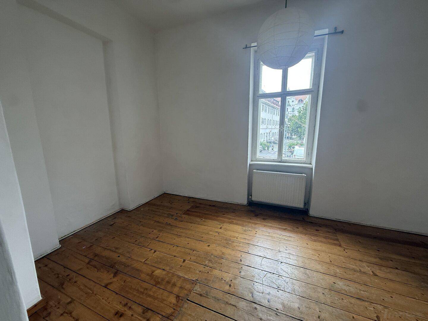 Helles Zimmer mit Holzdielenboden und einem großen Fenster, das einen Blick nach draußen bietet.