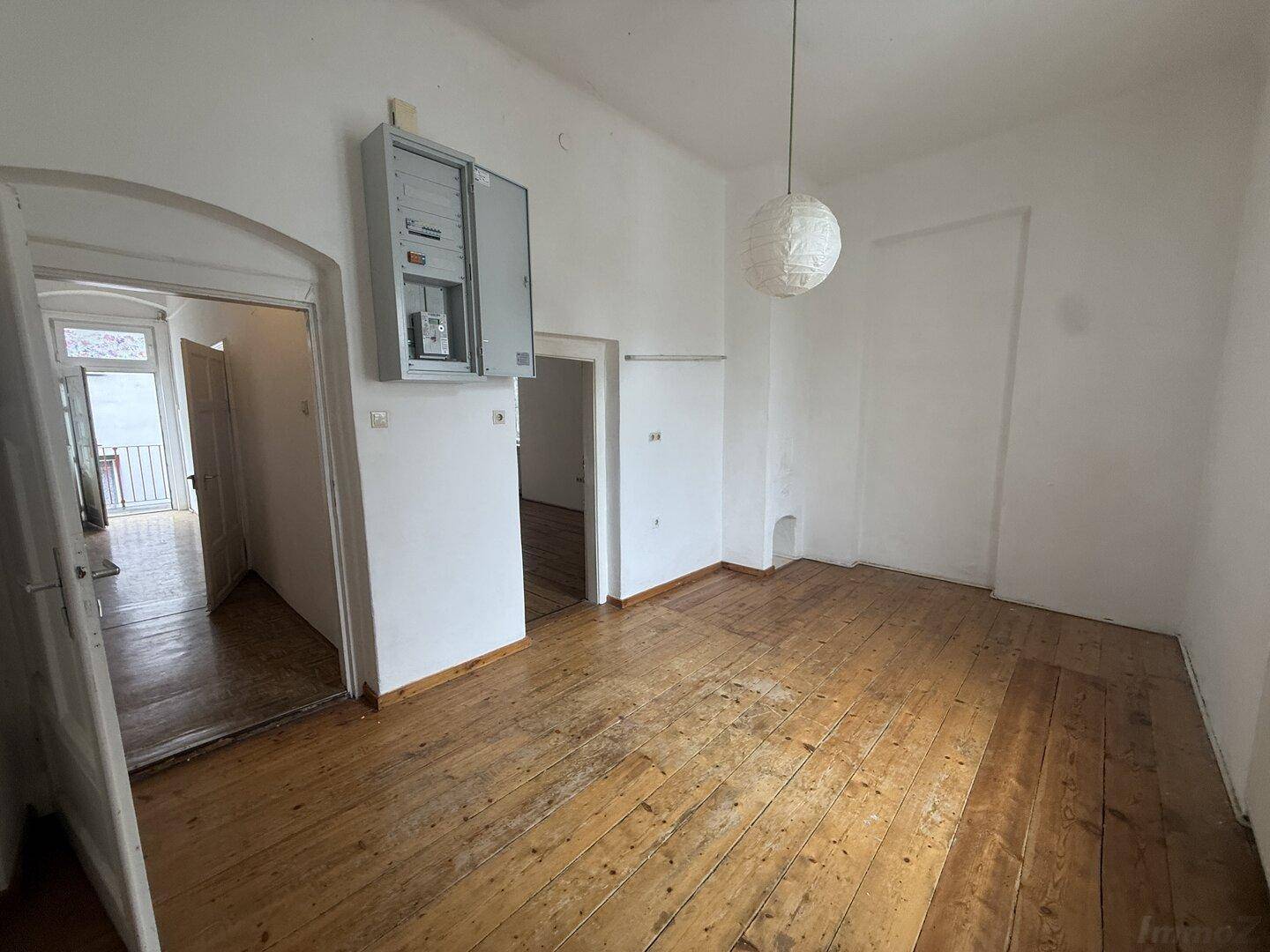 Geräumiges Zimmer mit Holzdielenboden und offenem Zugang zu einem weiteren Bereich.