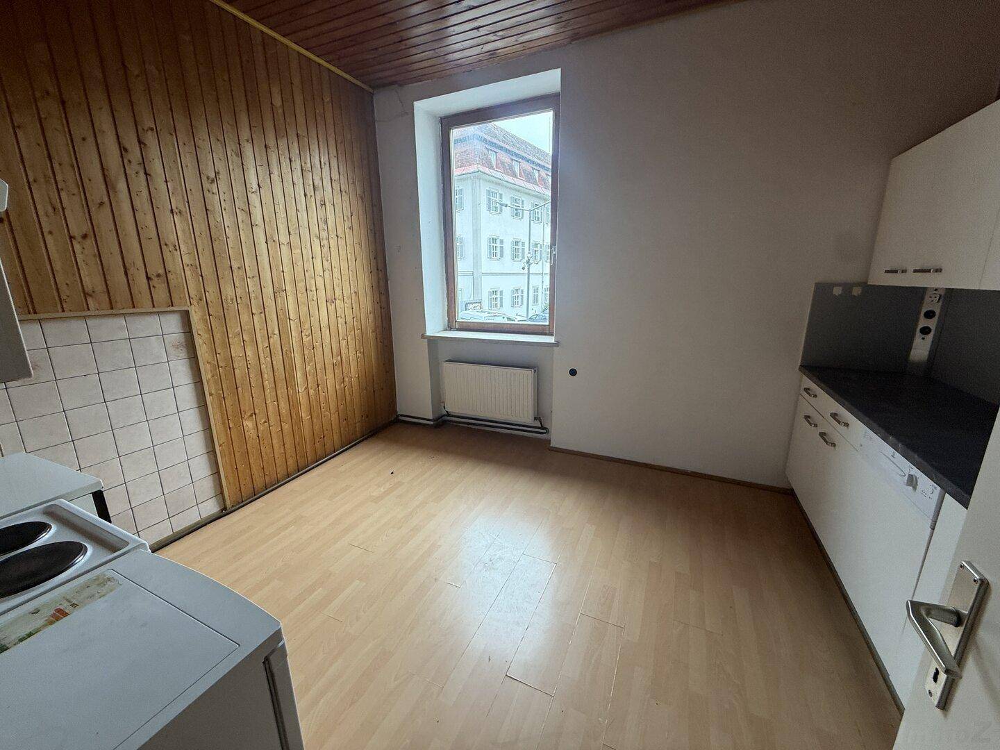 Küche mit Holzvertäfelung, Fenster und einfacher Küchenzeile, bereit für eine Modernisierung.