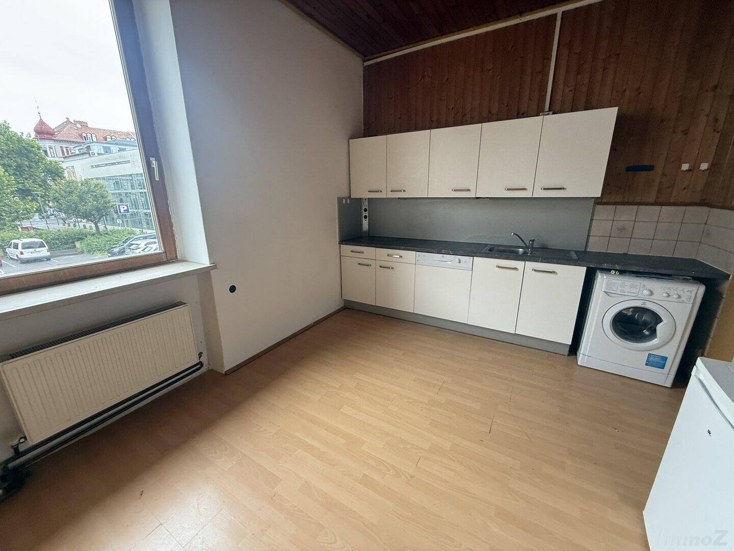 Helle Küche mit Holzvertäfelung, Einbauschränken und Blick auf die Stadt durch das Fenster.