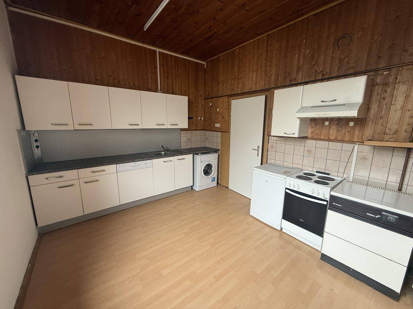 Küche mit Holzvertäfelung, Einbauschränken und Haushaltsgeräten, funktional und geräumig.