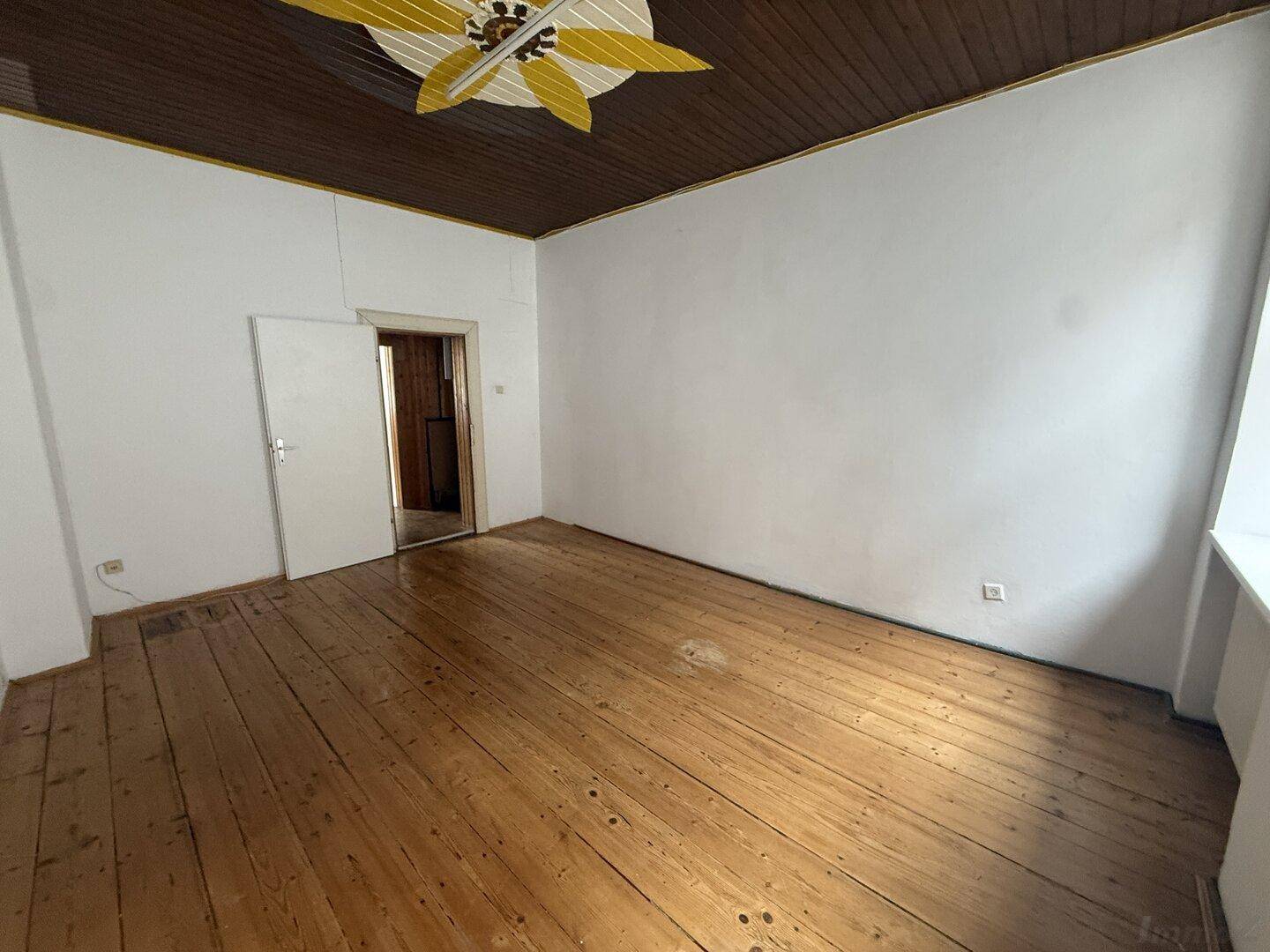Geräumiges Zimmer mit Holzdielenboden und Holzdecke, bietet Zugang zu einem weiteren Raum.