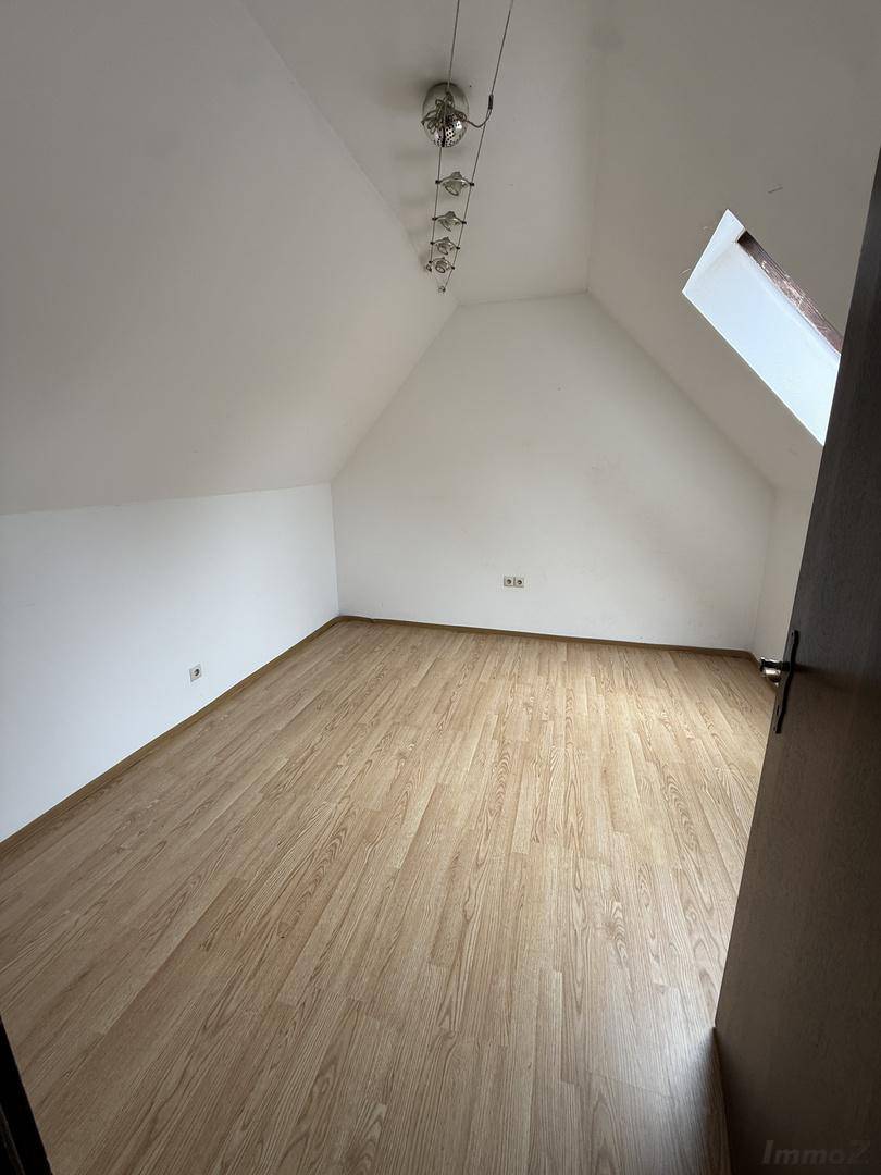 Geräumiges Schlafzimmer im Dachgeschoss mit Laminatboden, weiß gestrichenen Wänden und Dachfenster.