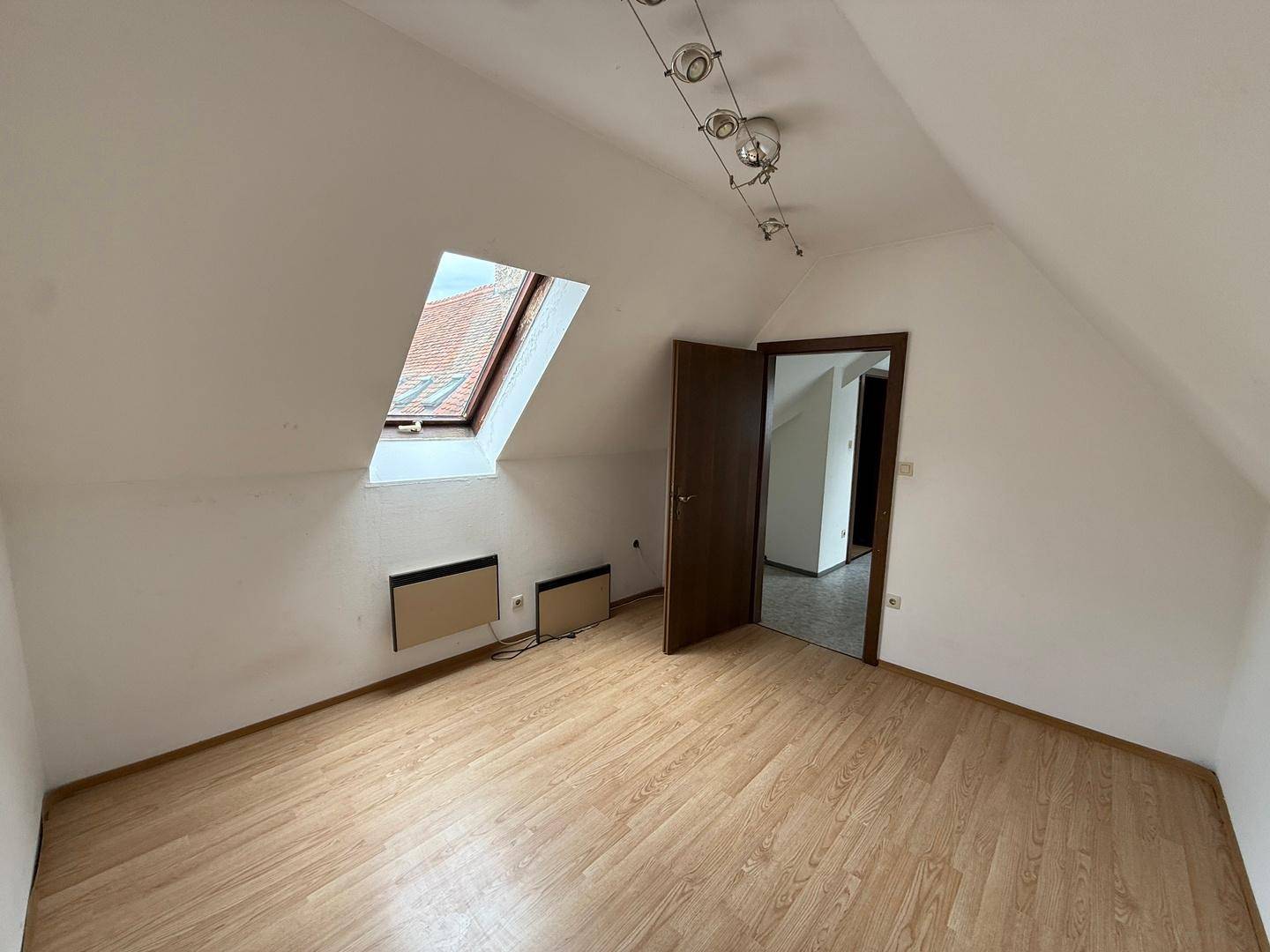 Helles Schlafzimmer im Dachgeschoss mit Laminatboden, Dachfenster und Zugang zu einem weiteren Raum.